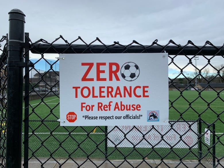 A sign attached to a fence at a soccer field reads "Zero tolerance for ref abuse. Please respect our officials." 