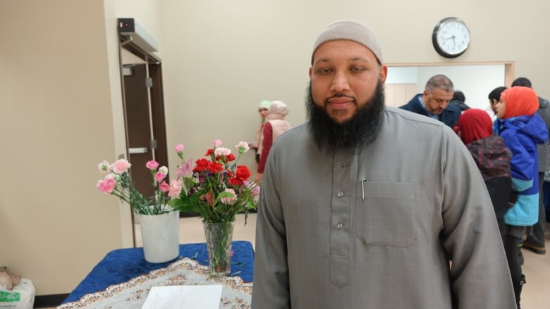 A Muslim man stands in a room and looks at the camera.