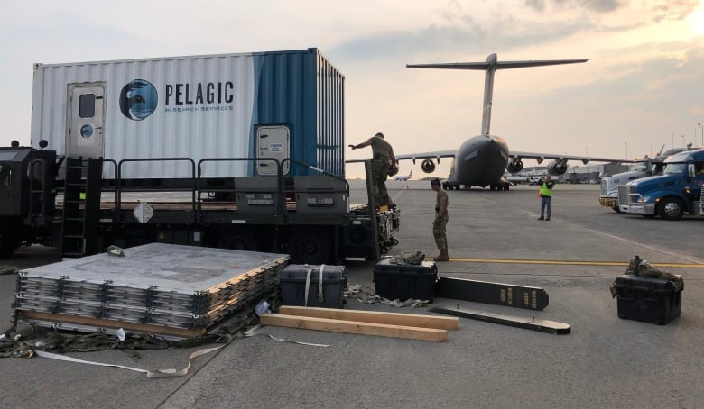 A shipping container with the word PELAGIC on the side, while a C17 aircraft waits in the background.