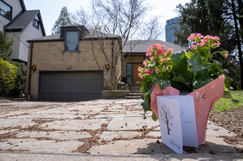 Flowers and a card sit on the pavement in the foreground, with a house in the background.