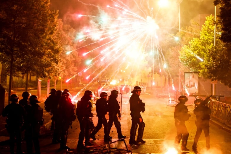 Fireworks go off as police officers stand in a group.