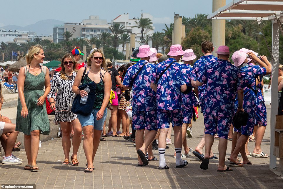 Three girls chuckle as they pass a group of pals in matching flamingo two-pieces and pink bucket hats