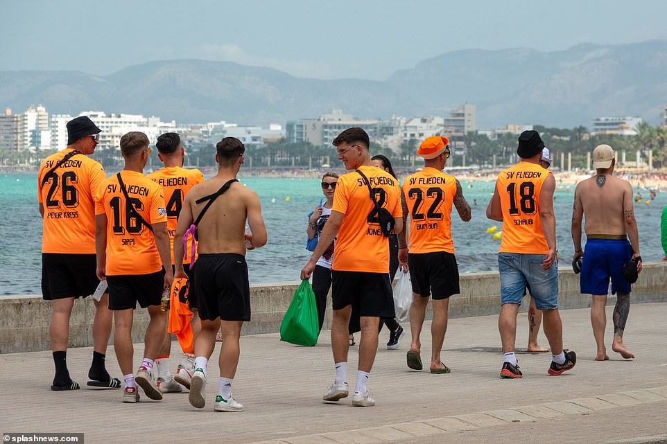 Another set of football fans wear the name of their German association football club on their backs as they strut alongside the beach