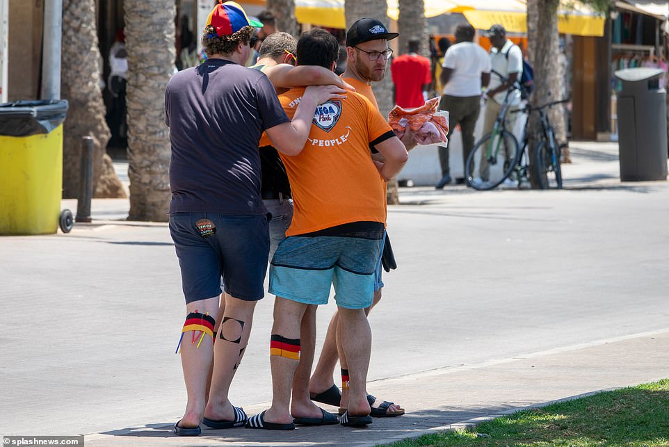 Four pals - all earing the German flag on their legs - help eachother down the street