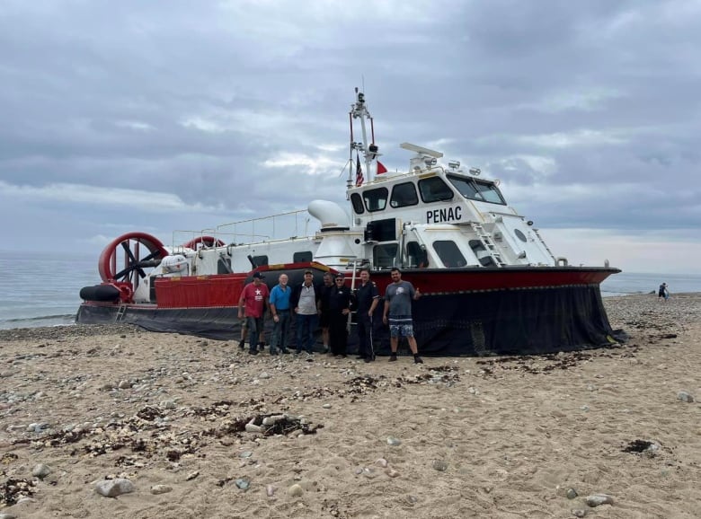 The Penac hovercraft sits on the beach, with a group of people standing in front for a pose.