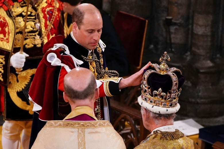  A man touches a crown on another man's head.