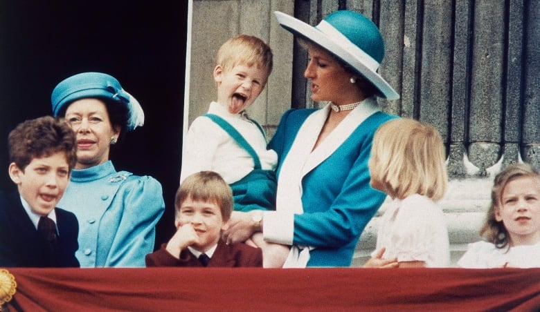 A child held by an adult sticks out his tongue as another children look on and other people stand around them.