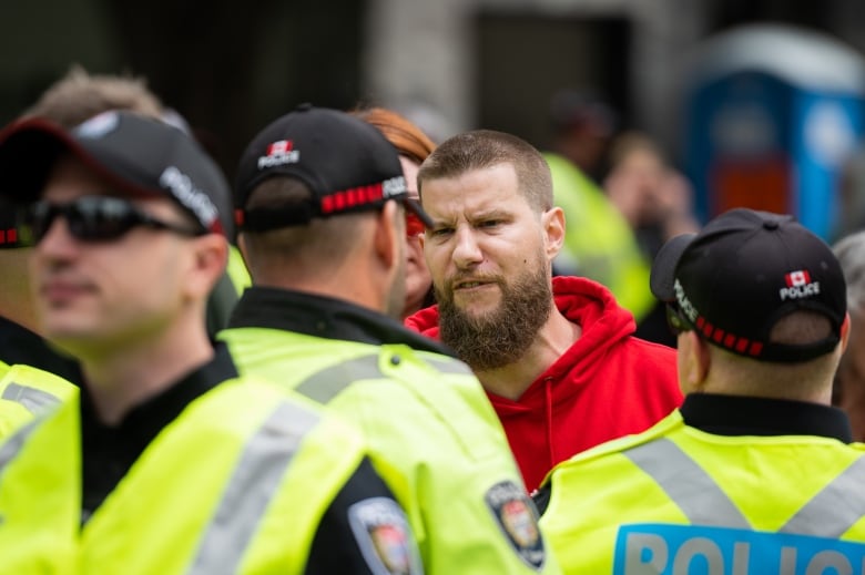 A man in a red hoodie stands in front of multiple police officers.