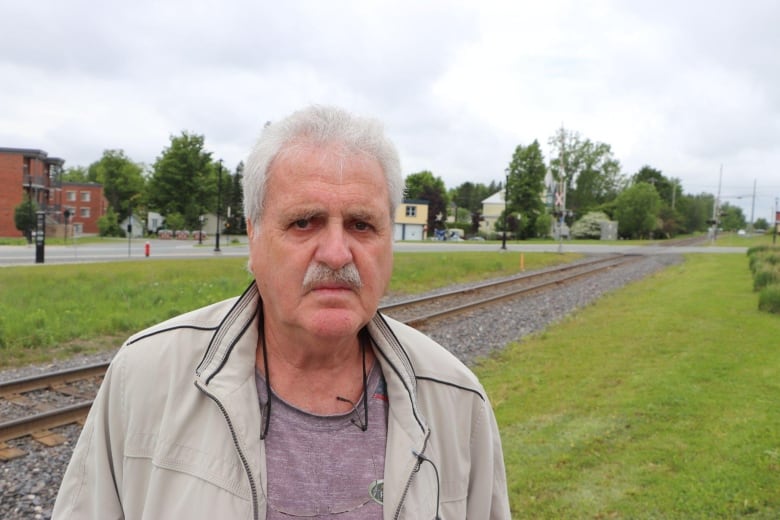 A man looks at the camera, standing in front of a train track.