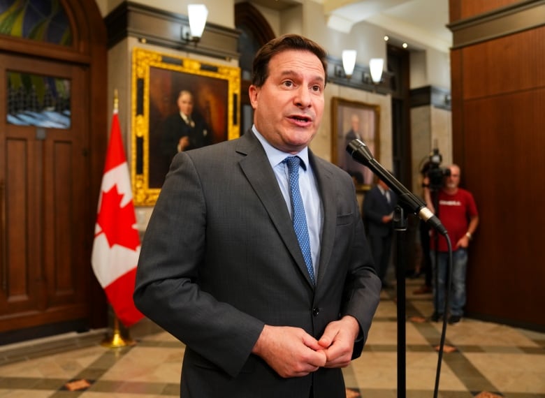 A man in a suit standing at a microphone in a foyer.