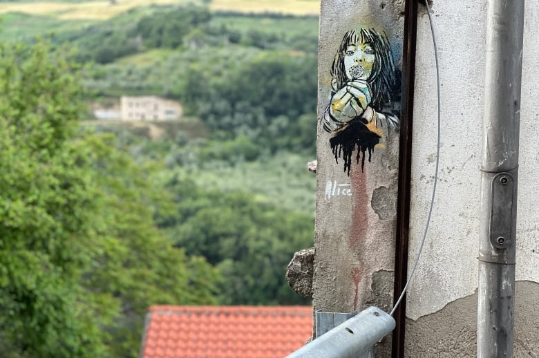 A small painting of a girl blowing a dandelion is shown on a wall of a stone building.