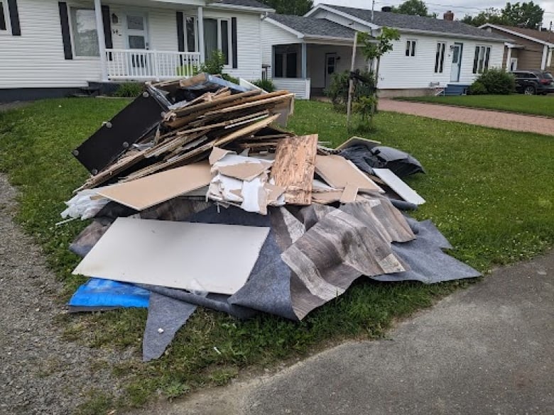 A pile of wood, flooring, and various materials piled at the curb of a house.