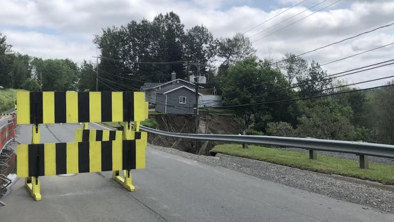 A road running alongside a hole caused by a landslide is blocked by a yellow and black barrier.