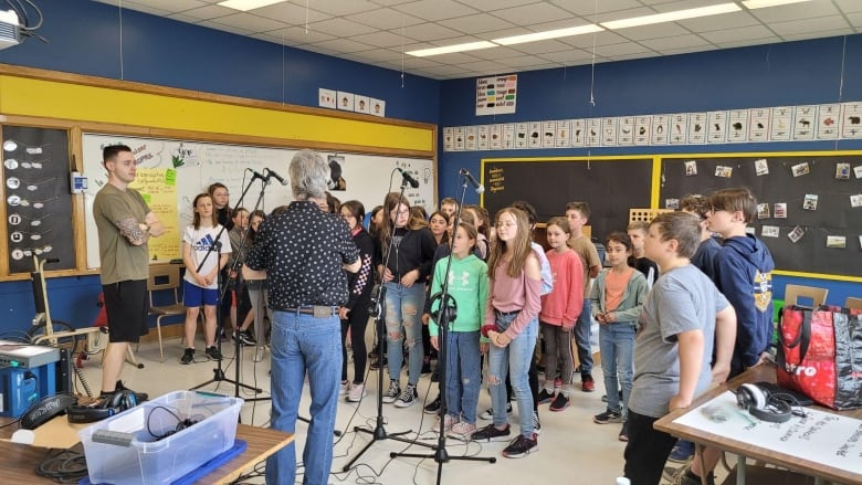 Students stand in a classroom in front of microphones.