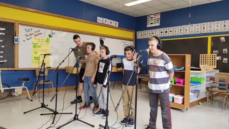 Four students stand in front of microphones in a classroom 