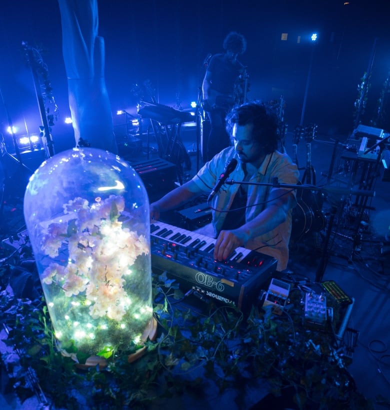 A musician plays at a keyboard on a dark stage.