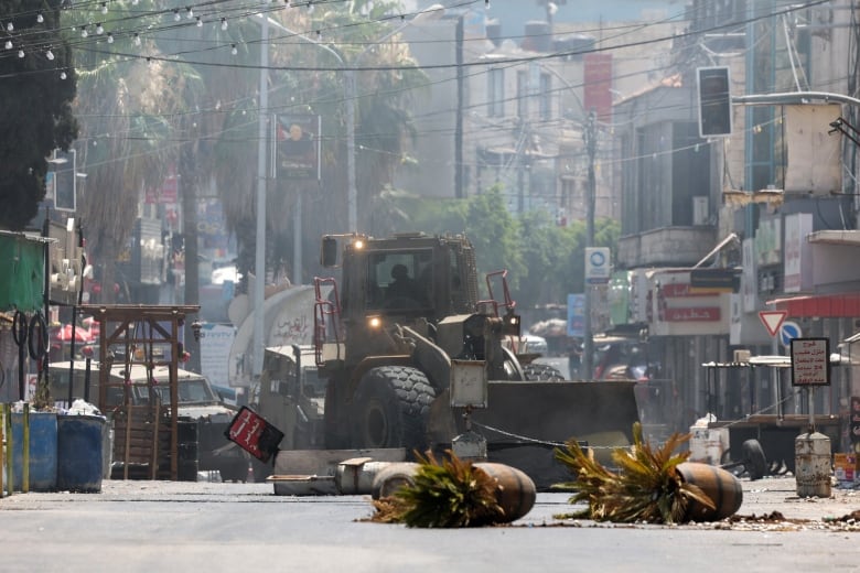 A bulldozer is seen on a street as debris is seen in the foreground.