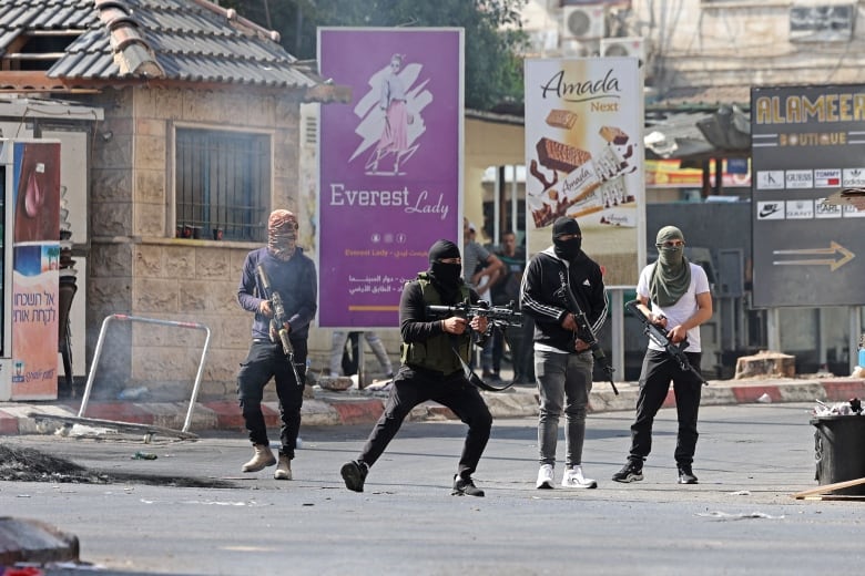 People armed with rifles and wearing fabric covering their faces are seen on a street. 