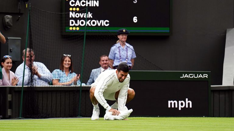 Novak Djokovic inspects the moisture on court and uses a towel to attempt to dry the grass during a rain delay in their match on day one of the 2023 Wimbledon Championships at the All England Lawn Tennis and Croquet Club in Wimbledon.