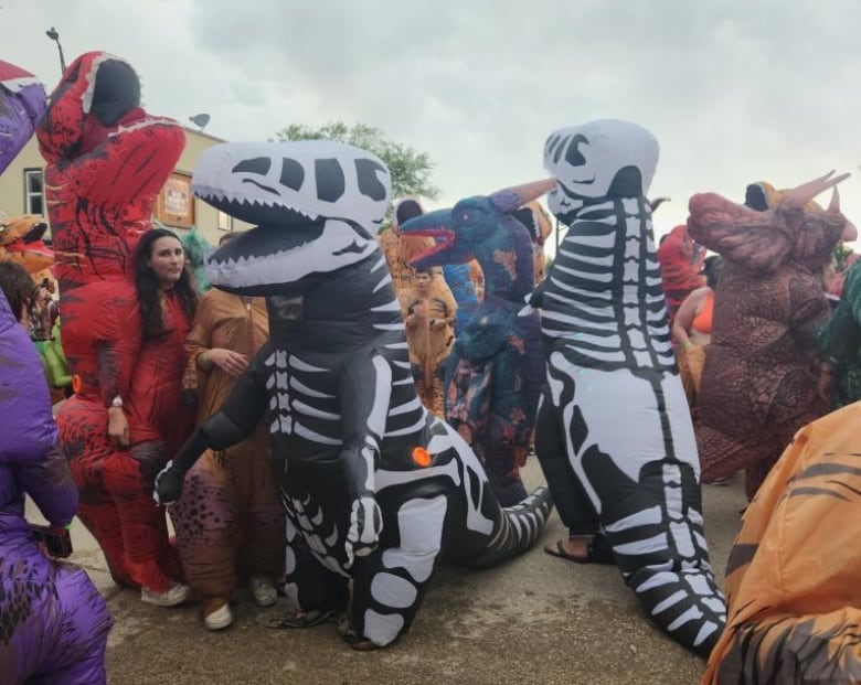 People in dinosaur costumes are wandering around on a crowded street in Dundurn.