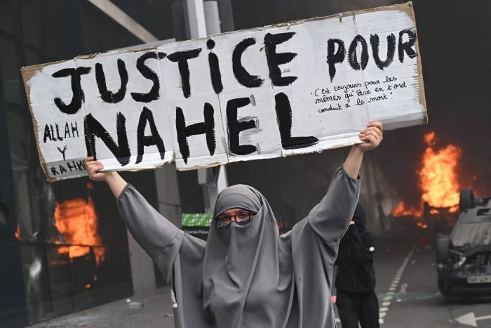 A demonstrator holds a banner reading ‘Justice for Nahel’ as cars burn in the street