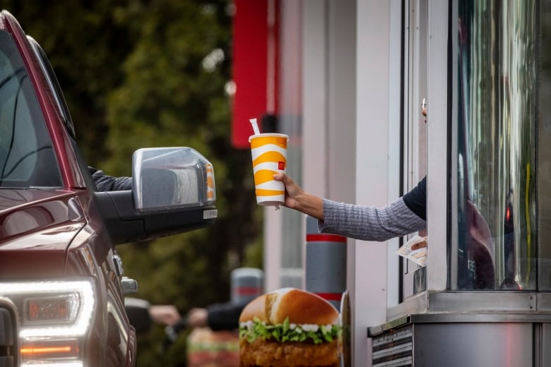 A food service worker hands a McDonald's branded cup to a driver through a drive-thru window.