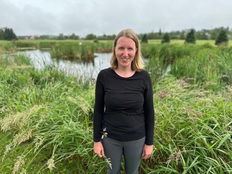 A woman stands in front of a wetland 