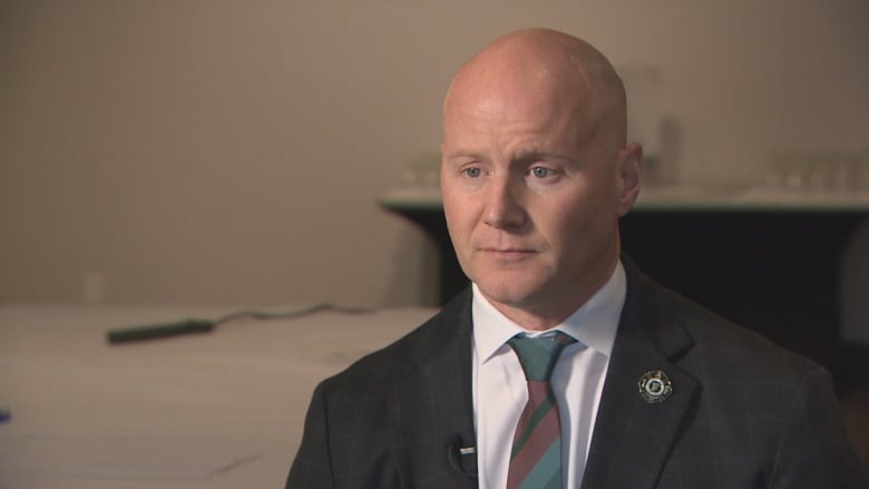 A bald man in a suit and tie with an IAFF pin sits for an interview.