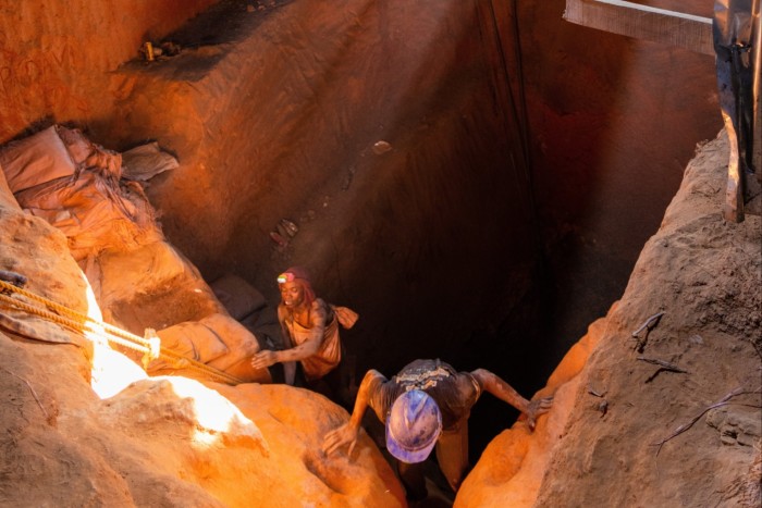 Two miners crawl out of a hole in the ground