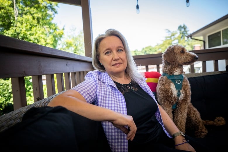 A white woman smiles for a photo with her dog while sitting on a patio.