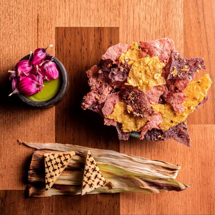 Chips, raw red onions in separate plates and two small triangular pieces of bread on top of corn husk