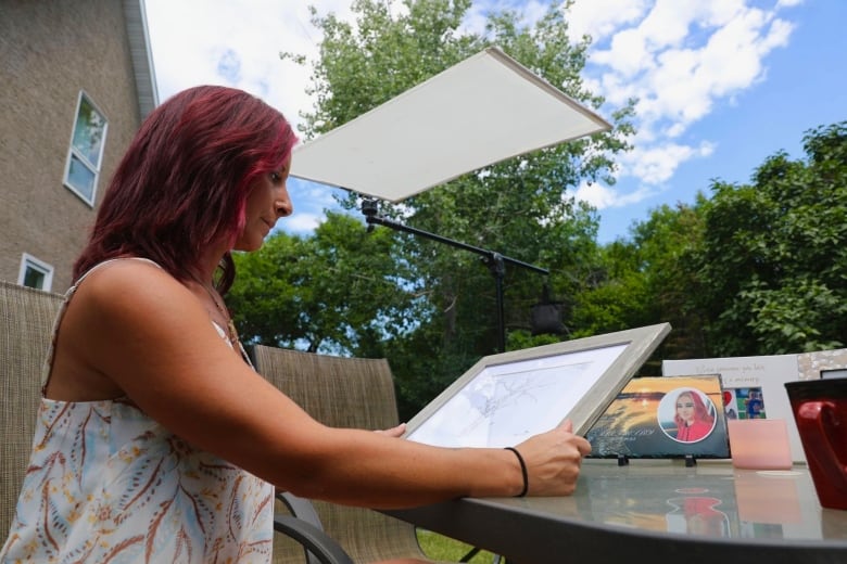 A woman with red hair looks at a framed drawing. 