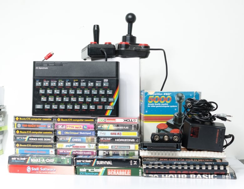 A plastic black keyboard with a rainbow logo on it next to a stack vintage games and a couple joysticks.