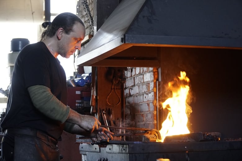 Man working metal near fire.