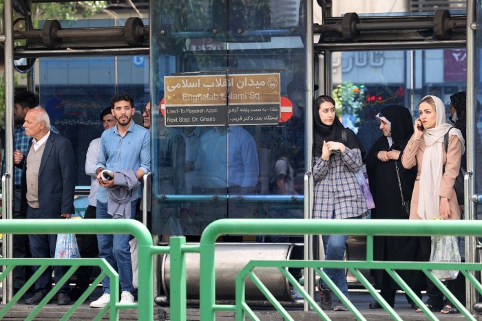 People gather at a bus stop in Tehran in May