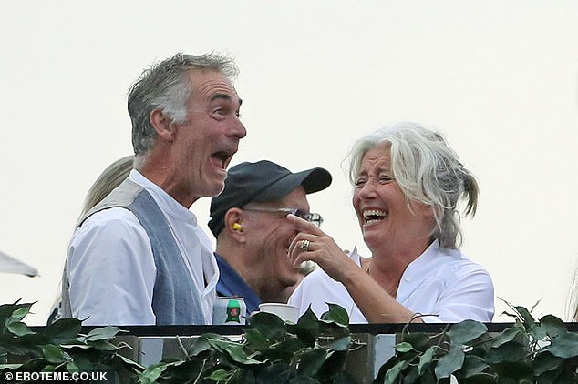 Happy: She sported a casual figure for the afternoon, wearing a half buttoned white flowy shirt and chic multicoloured headband alongside husband Greg Wise (Left)