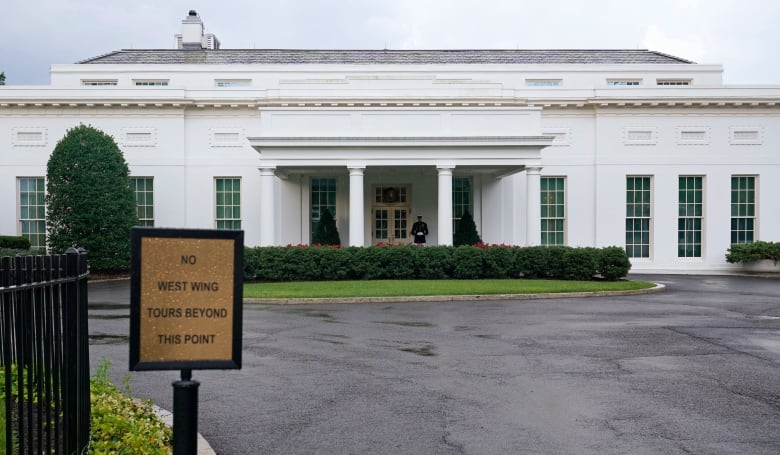 The White House is seen in the background, with a sign that reads "NO WEST WING TOURS BEYOND THIS POINT" in the foreground.