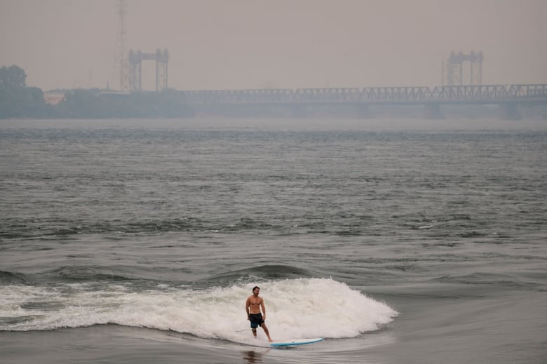 A surfer rides a wave in Montreal amid smokey skies.