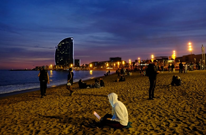 A woman typing on a laptop on a beach in Barcelona, Spain.