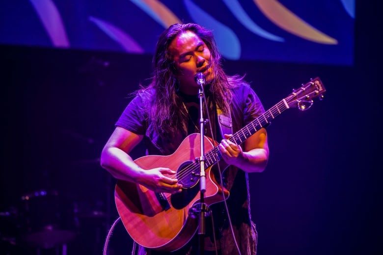 Oji-Cree singer Aysanabee sings onstage with his guitar.