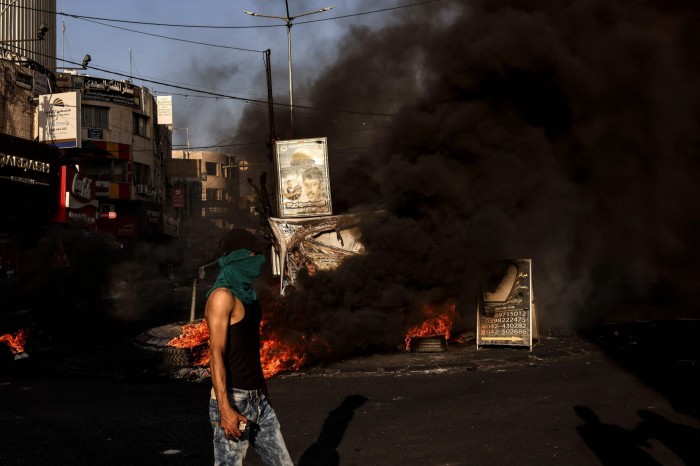 A masked man walks near a fire during clashes with the Israeli army in the occupied West Bank city of Jenin this month