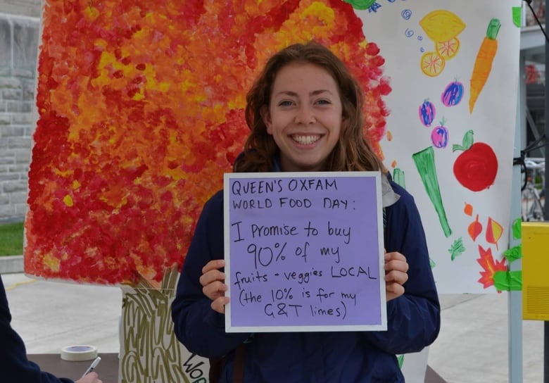 A woman smiles at a camera while holding up a sign that says "I promise to buy 90% of my fruits and veggies LOCAL."