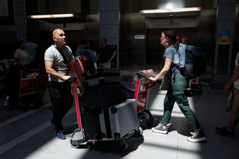 Travellers pushing luggage carts pass each other.