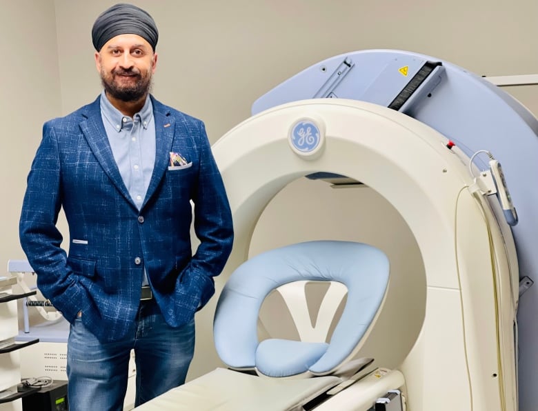 Dr. Anmol Kapoor stands beside a blue and white machine used in the scans.