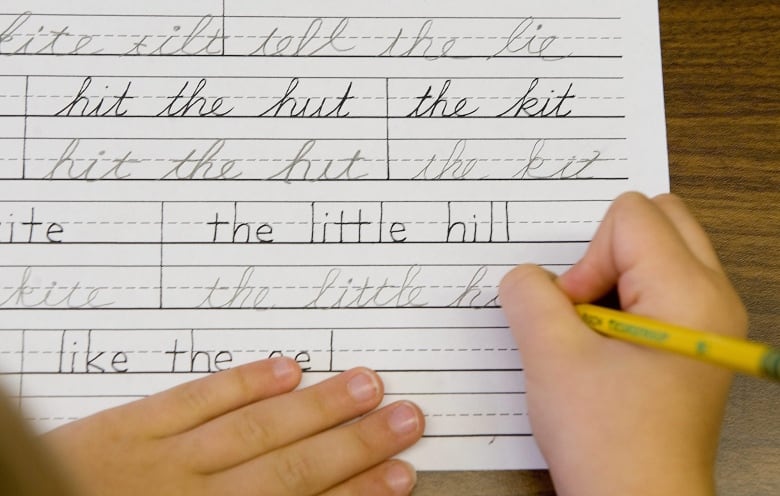 A kid's hands on a piece of paper, holding a pencil and writing in cursive.