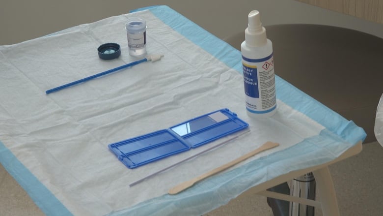 A Pap test that includes a spay bottle, two small wands and a blue container along with  an HPV test sit on the counte.