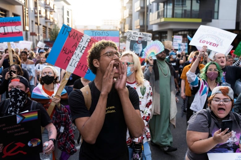 A crowd of people with trans flags and signs that say 'Trans Rights are Human Rights' march in the streets.