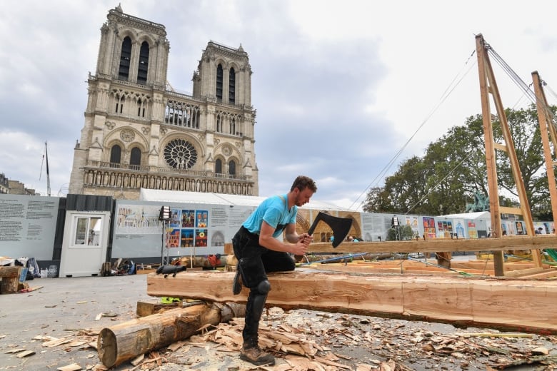 man cutting wood beam in front of cathedral.