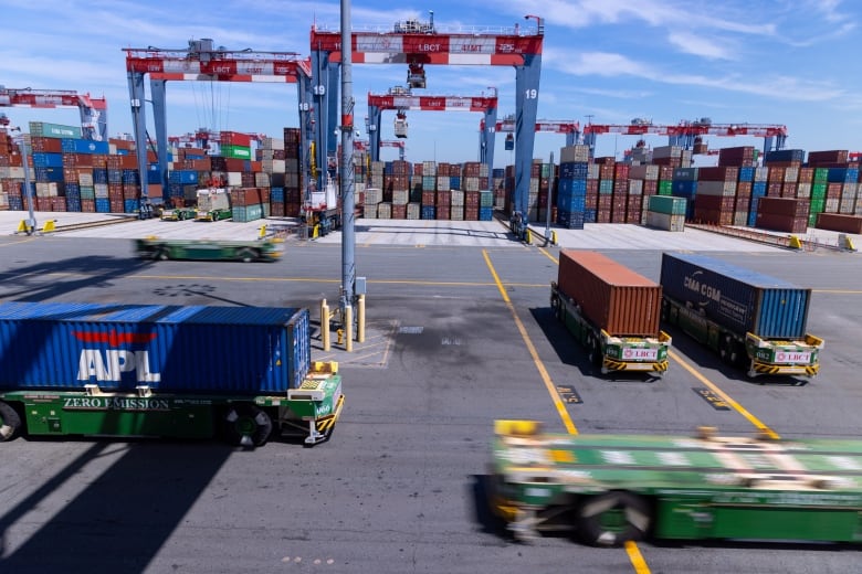 Driverless flatbed vehicles, carrying large metal shipping containers, move about a port.