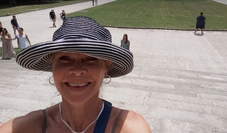 Woman in wide-brim hat stands in front of expansive palace garden.